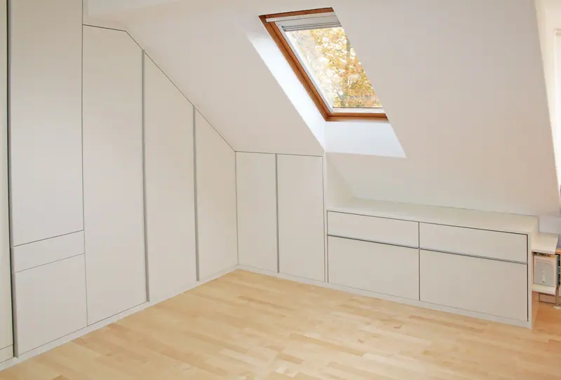 Weißer Einbauschrank mit Schubladen unter einer Dachschräge neben einem Dachfenster