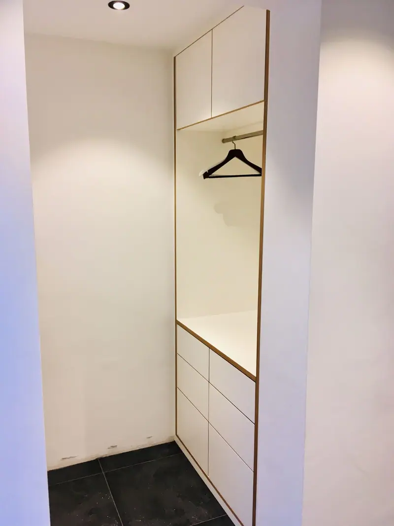 Raumhoher weißer Einbauschrank mit Garderobenstange und Schubladen in einer Nische