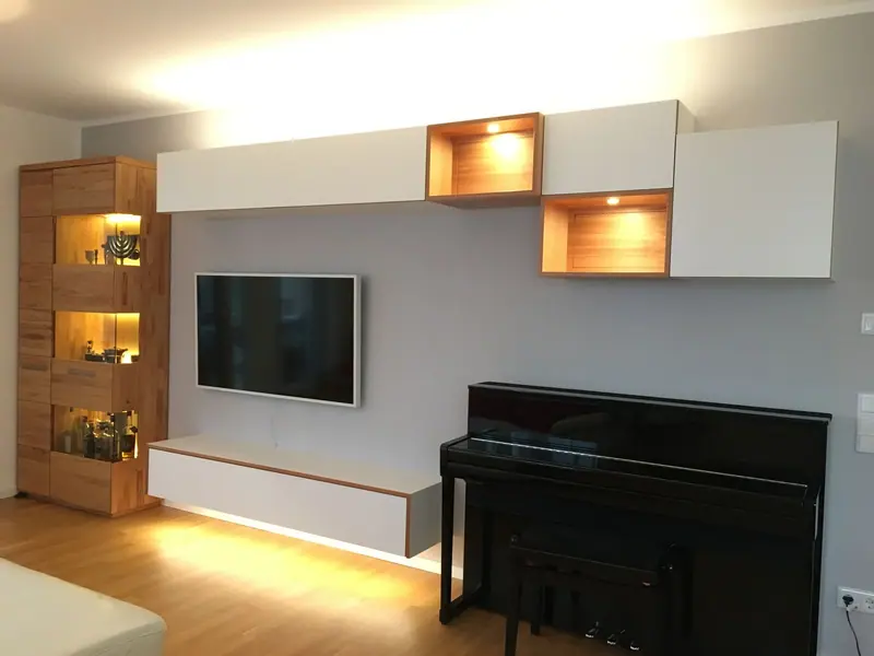Weiße Wohnwand mit Holzfächern und indirekter Beleuchtung hinter einem Fernseher